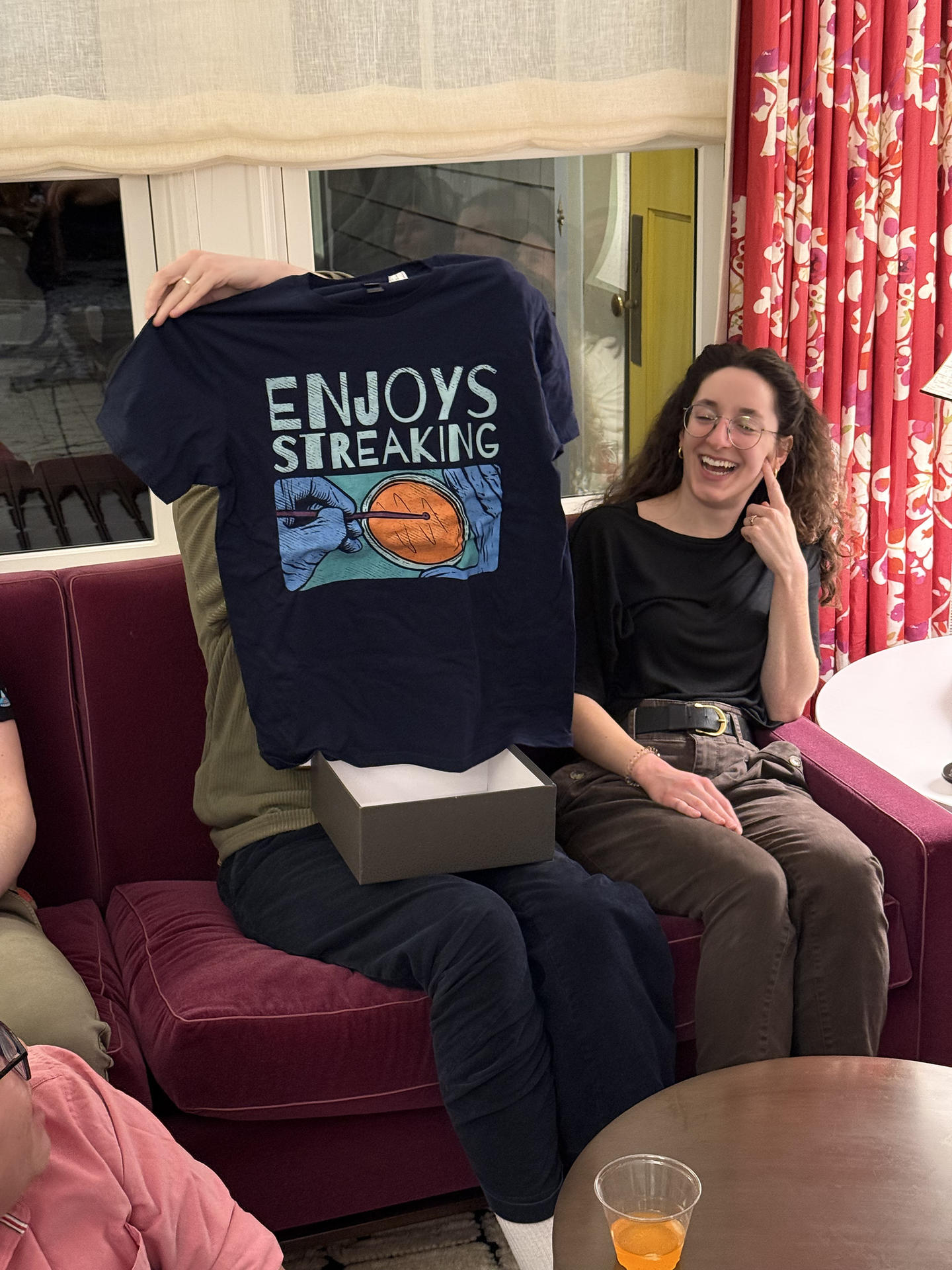 A person holding up at t-shirt that says "ENJOYS STREAKING", referring to streaking out bacteria